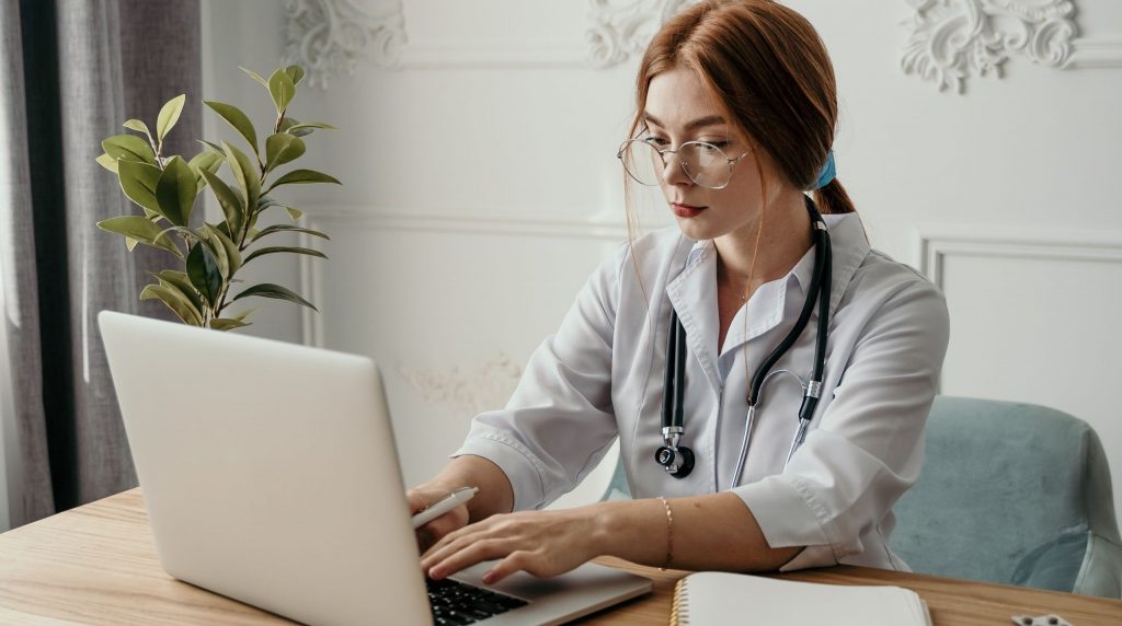jeune médecin en blouse tapant sur un ordinateur portable à son bureau