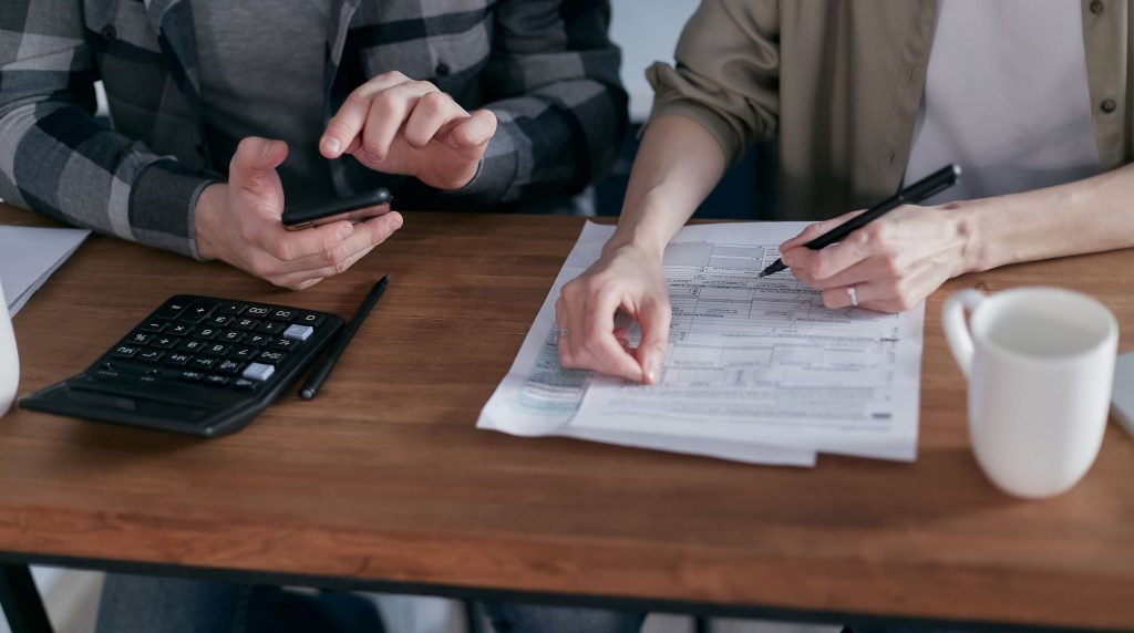 deux personnes remplissant un formulaire, calculatrice et téléphone sur la table