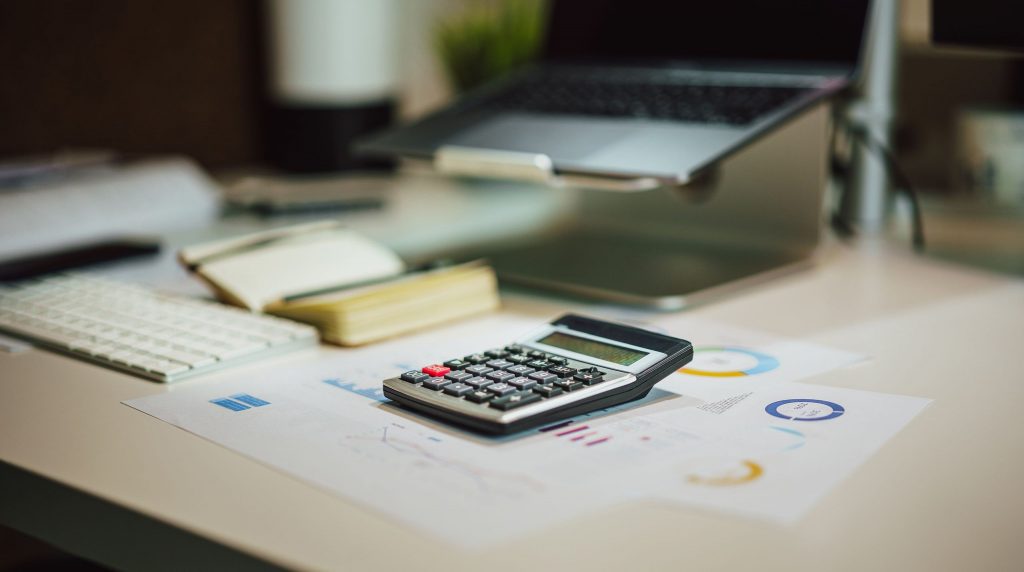 calculatrice posée sur des documents imprimés, ordinateur portable en arrière-plan