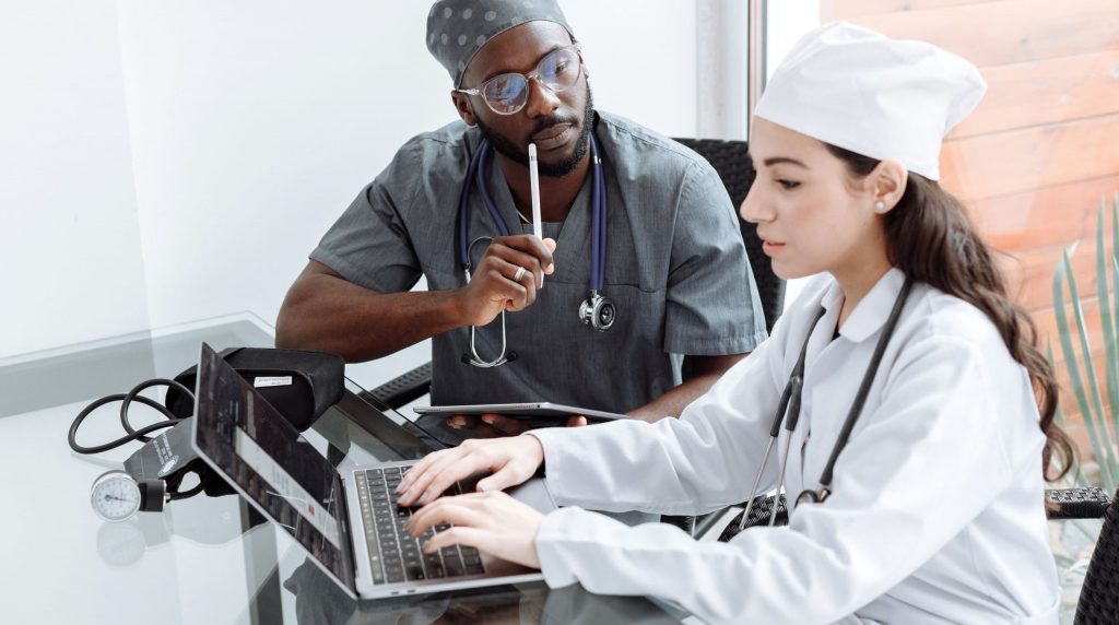 deux médecins, dont l'un en tenue de bloc, travaillant ensemble sur un ordinateur portable