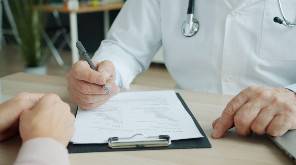 médecin annotant un document sur porte-bloc, face à son interlocuteur