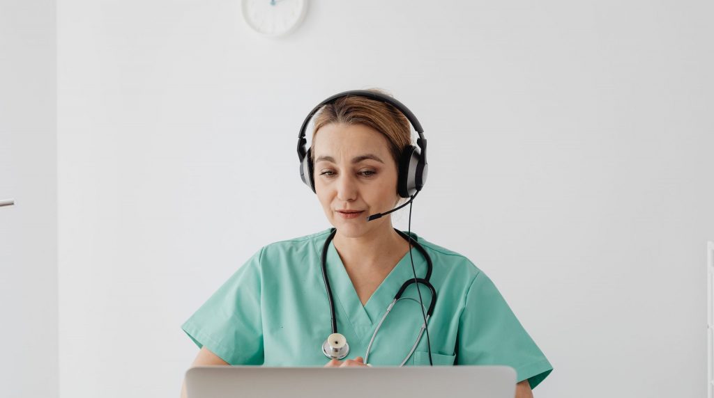 médecin en tunique, casque micro sur la tête, face à un ordinateur portable