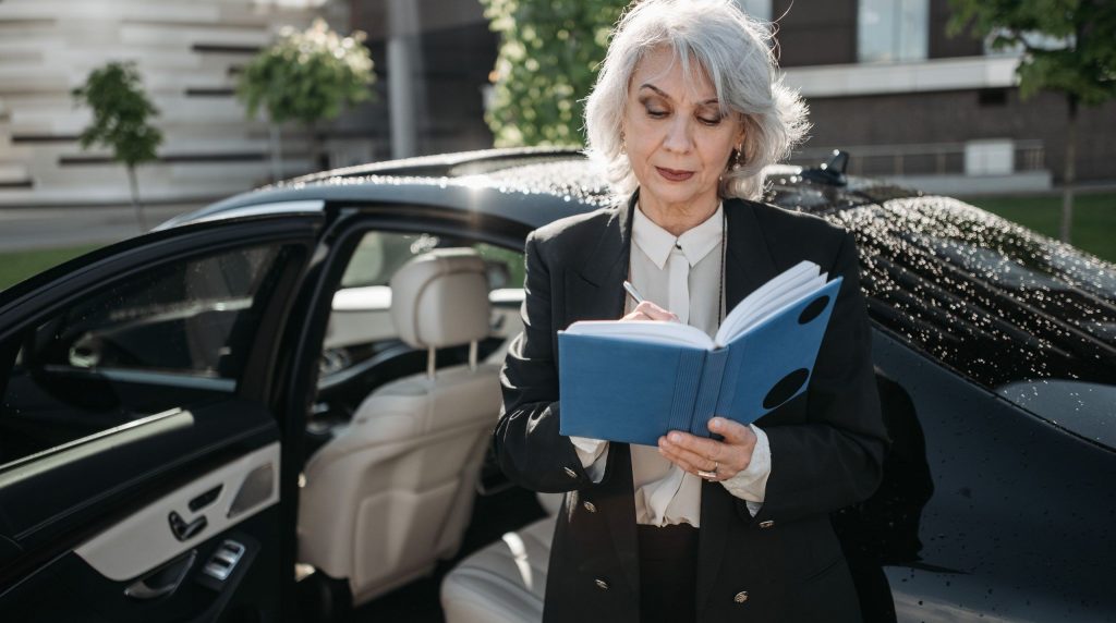 professionnelle notant ses kilomètres dans un carnet, portière de sa voiture ouverte